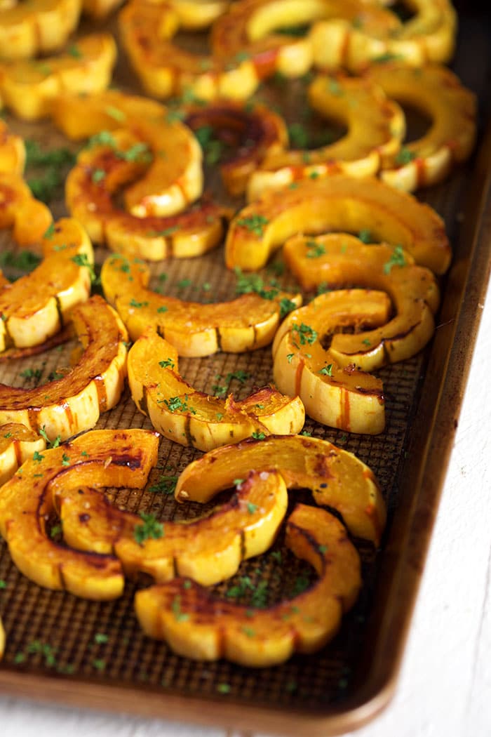 Delicata squash on a baking sheet with parsley sprinkled over it.