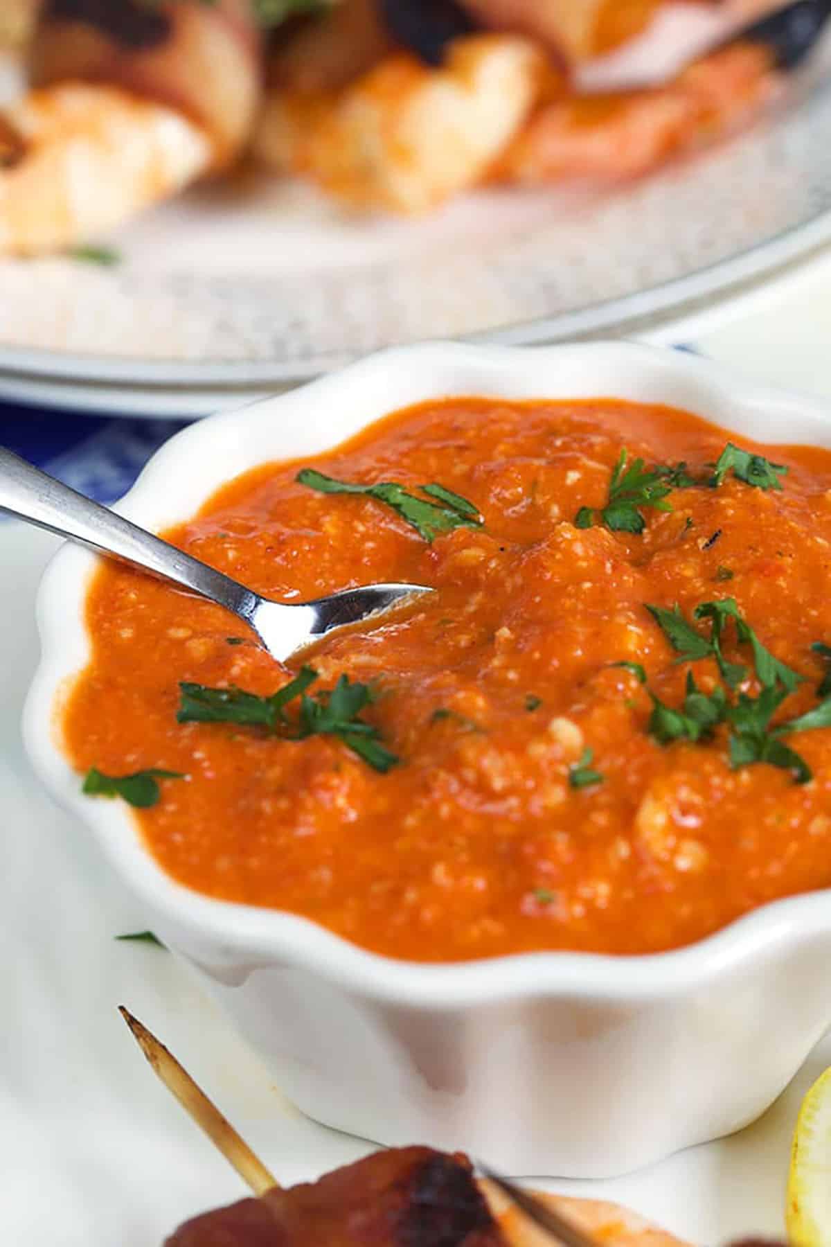 Romesco Sauce in a white bowl with a silver spoon in it.