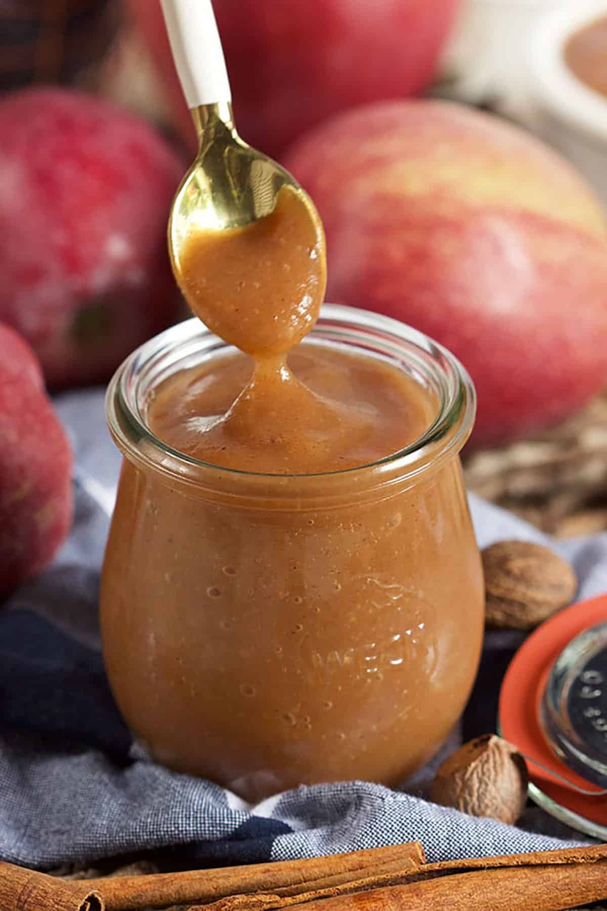 Apple butter in a weck tulip jar with a spoon and apples in the background.