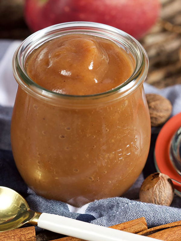 apple butter in a jar with a blue napkin underneath and a white spoon in front of it.