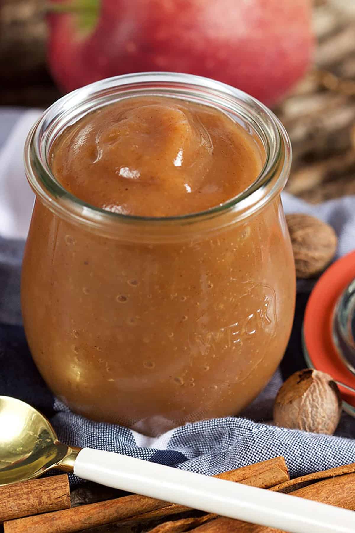 apple butter in a jar with a blue napkin underneath and a white spoon in front of it.