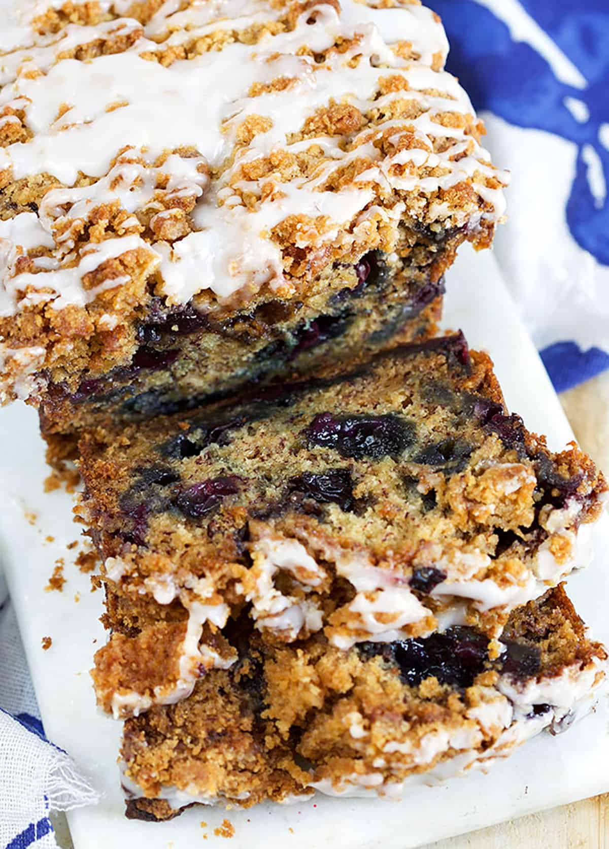 Blueberry Banana Bread with streusel and glaze sliced on a marble board with a blue napkin