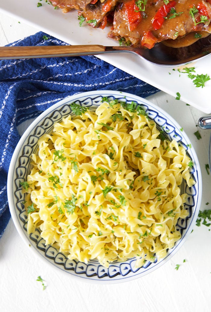 Overhead buttered egg noodles in a blue and white bowl on a white background with a blue napkin.