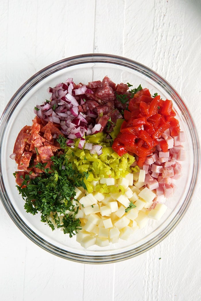 Ingredients for hoagie dip in a glass bowl on a white background.