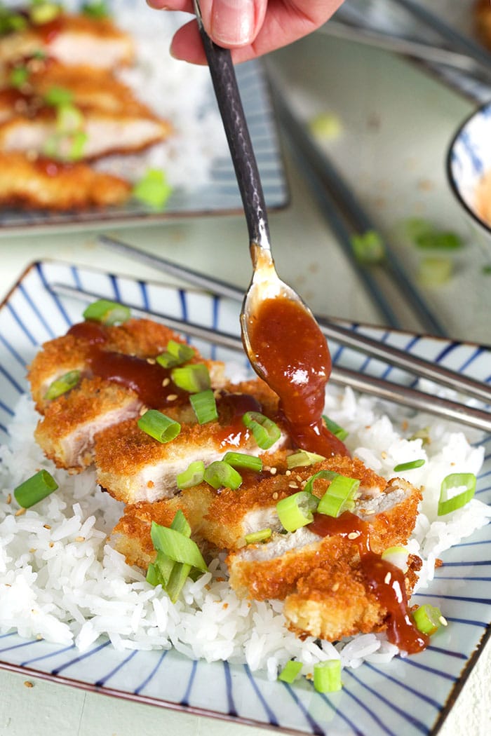 Tonkatsu on a bed of rice with sauce being drizzled with a spoon.