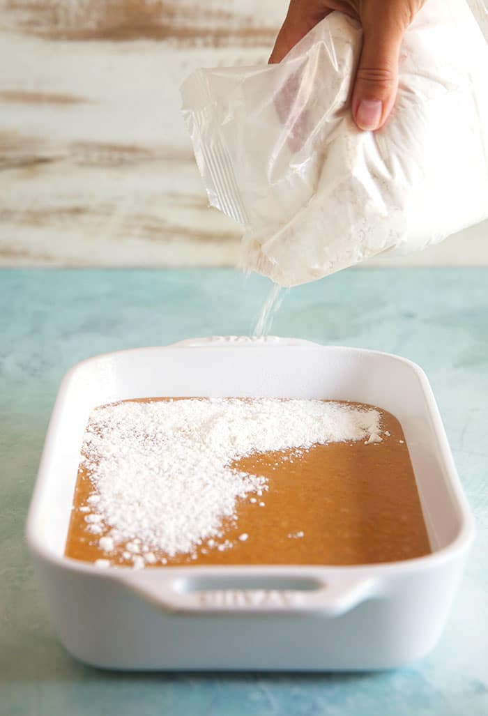 Cake mix being sprinkled over pumpkin filling in a white baking dish.