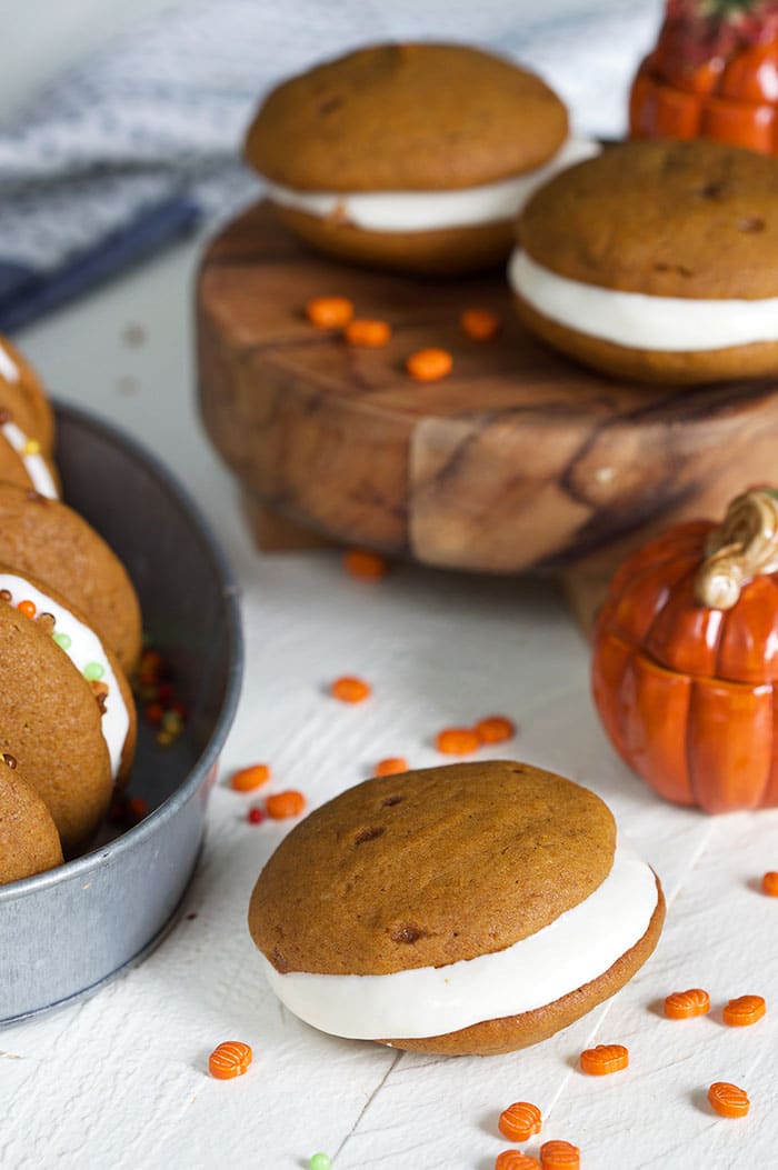 Pumpkin whoopie pies on a wood block with a ceramic pumpkin in front of them.