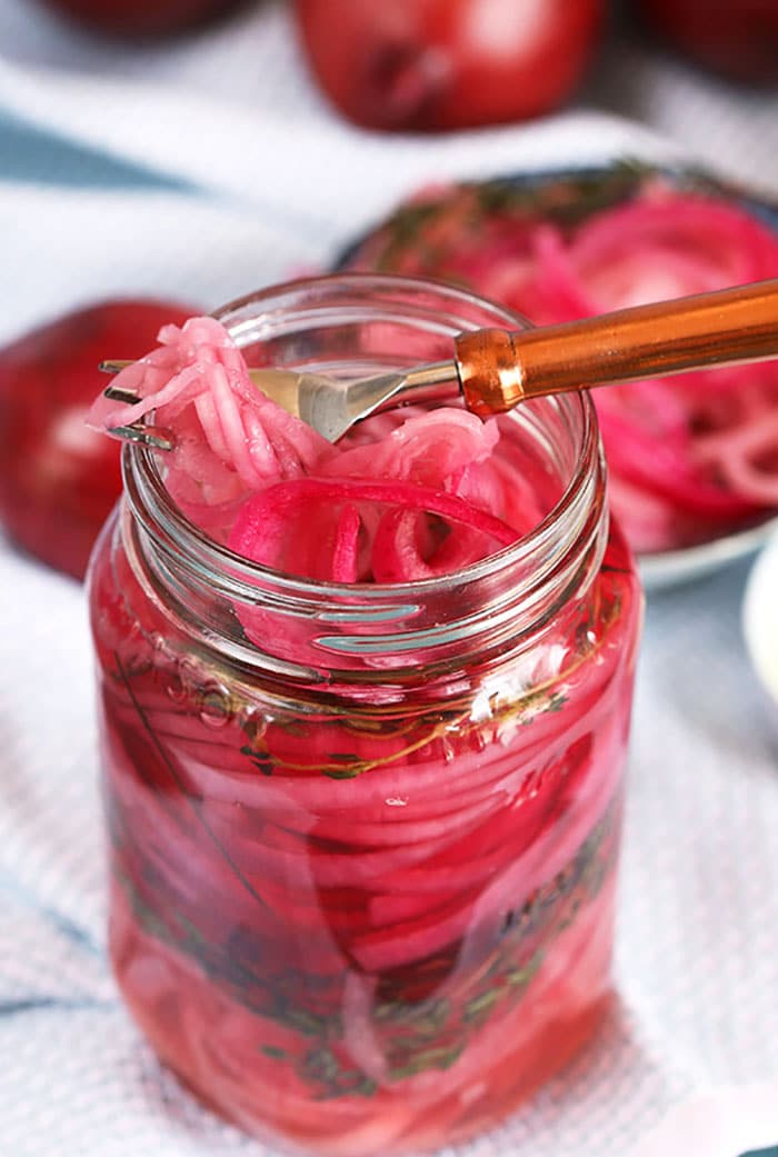 Pickled red onions in a jar with a copper fork on top.