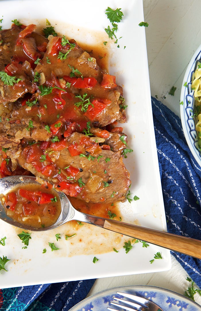 Swiss steak on a white platter with a spoonful of gravy.