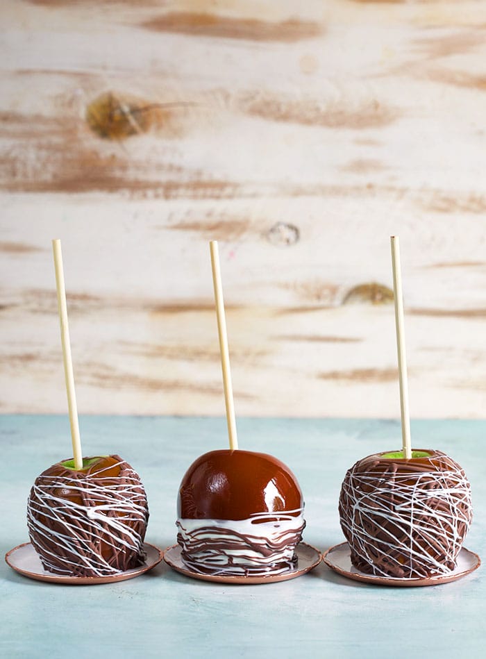 Three caramel apples in a row on a blue background.