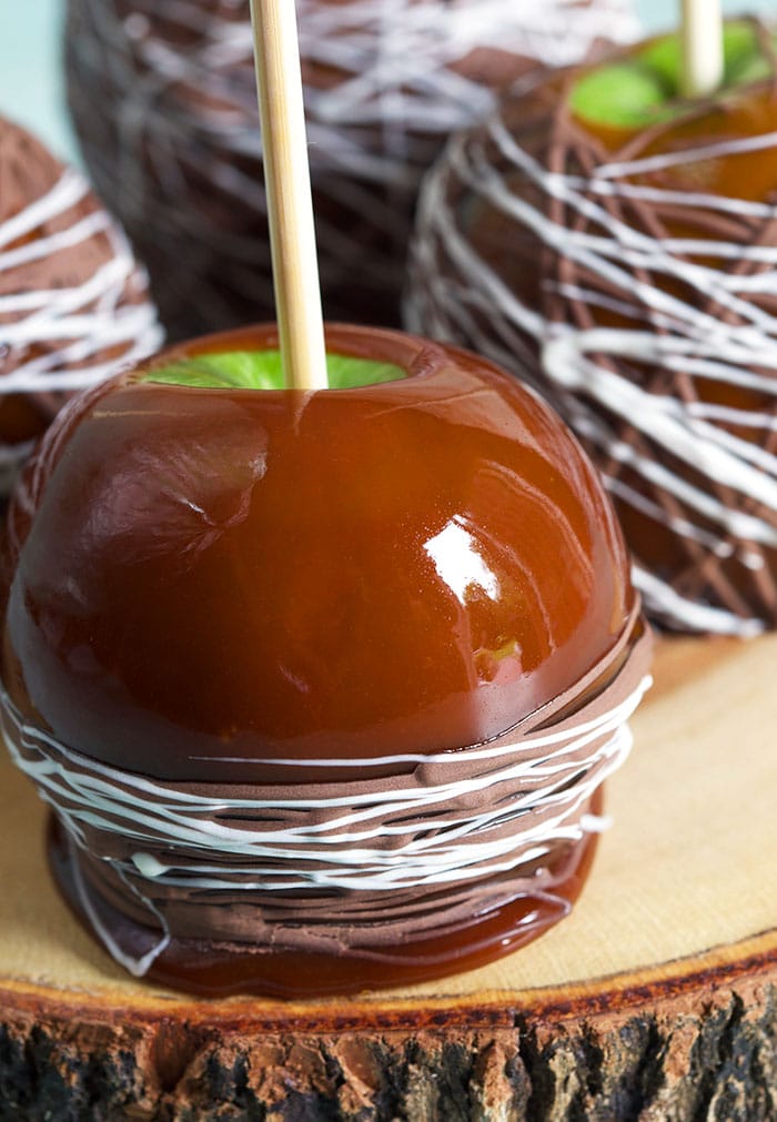 Close up caramel apple with chocolate drizzle on a piece of wood.