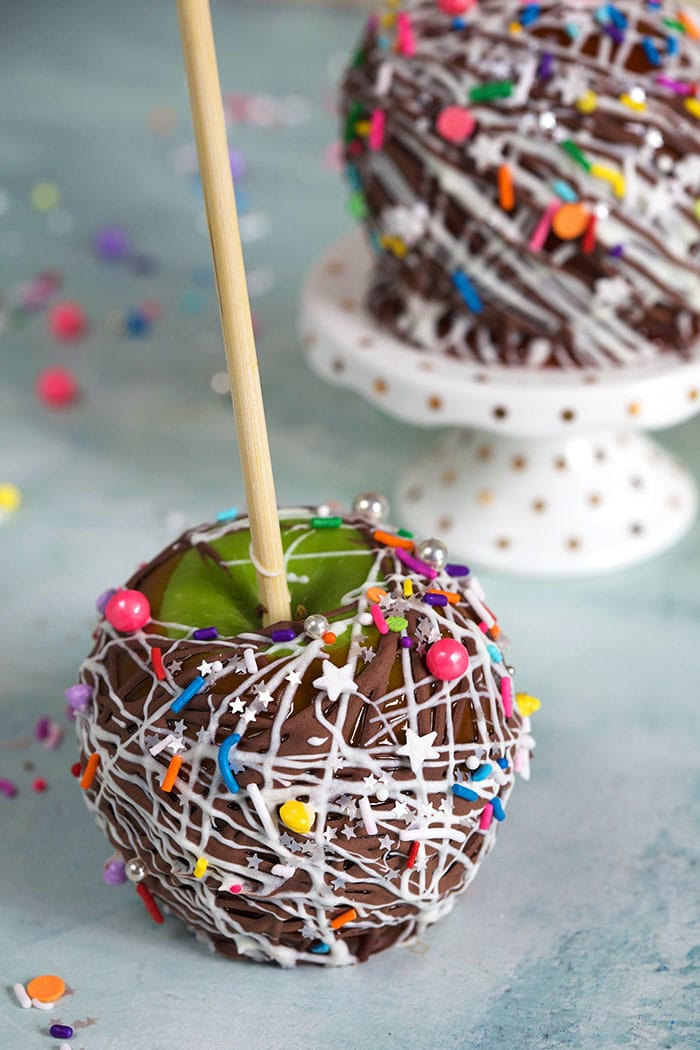 Caramel apple with unicorn sprinkles on a blue background.