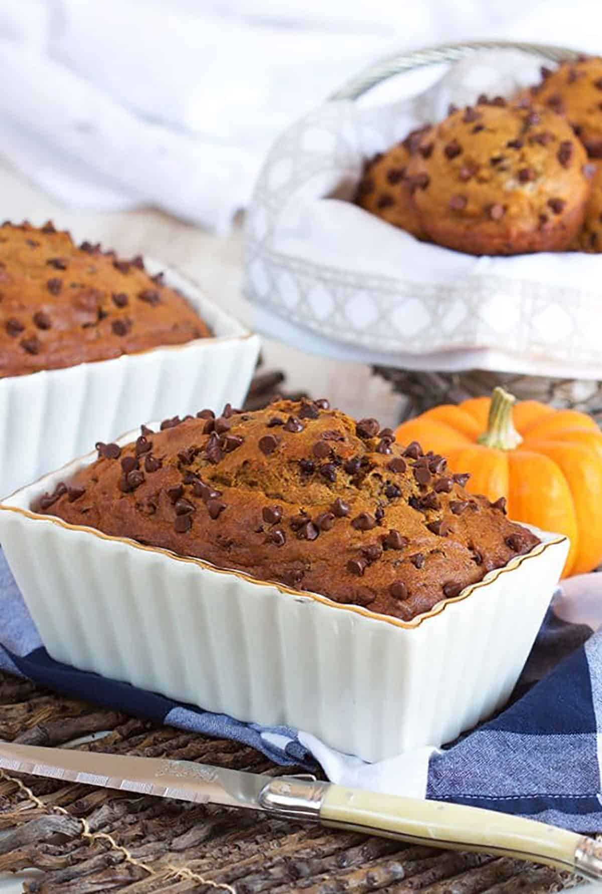 Chocolate Chip Pumpkin Bread in a white loaf pan with a pumpkin behind it.