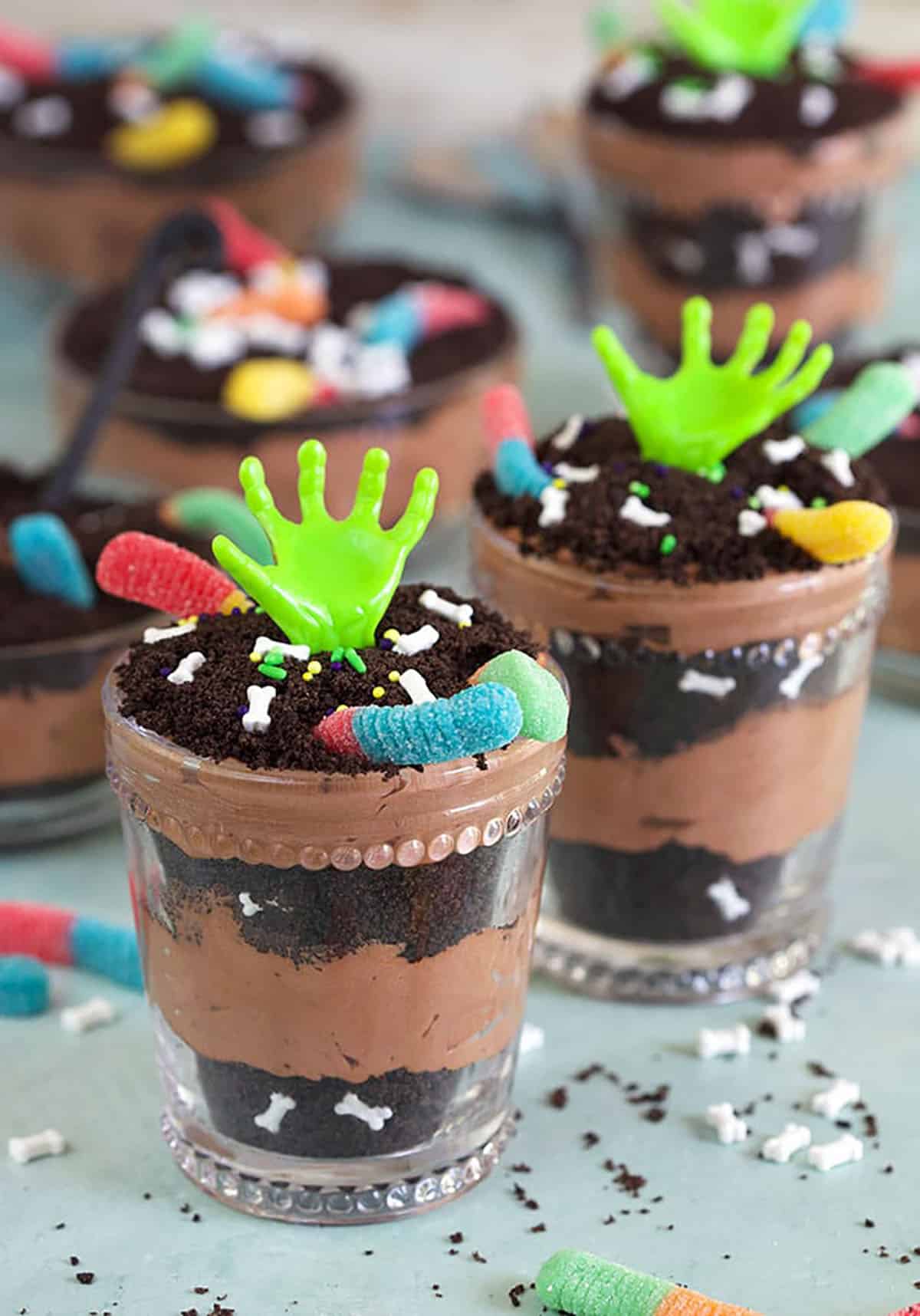 Dirt pudding cups in glasses with zombie hands.