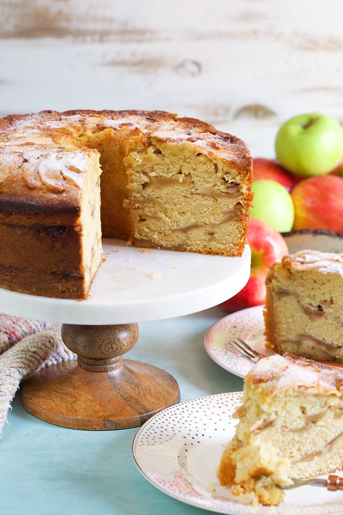 Jewish apple cake with two slices cut out and apples in the background.