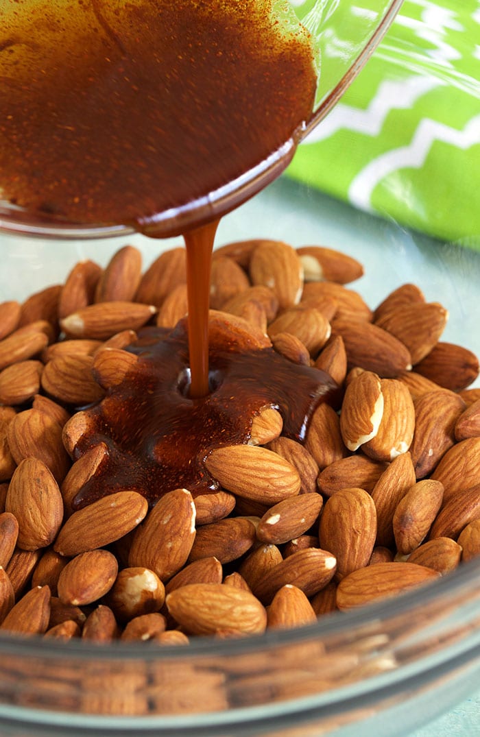 syrup being poured over almonds in a glass bowl.