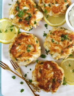 crab cakes on a white platter with gold forks.