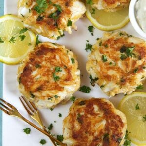 crab cakes on a white platter with gold forks.