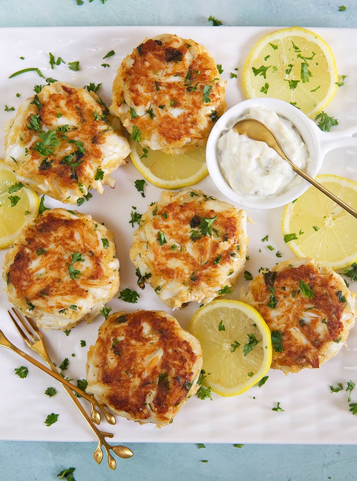 best crab cakes on a white platter with a bowl of tartar sauce.