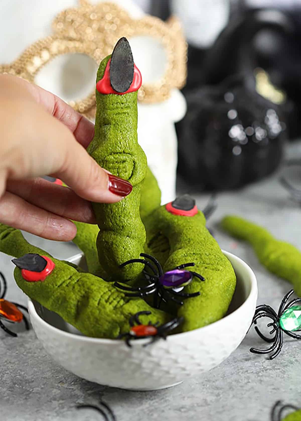 A hand holding a witch finger cookie over a bowl.