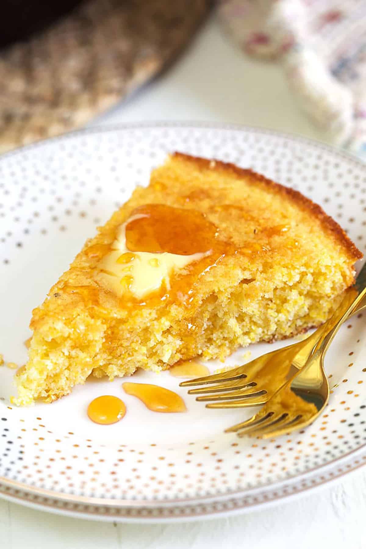 A piece of cornbread is garnished with butter and honey on a white plate.