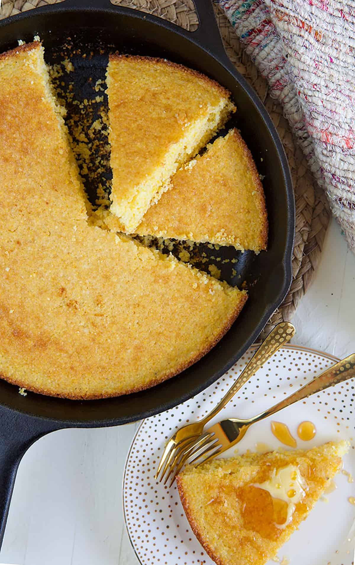 Two slices of cornbread are in a skillet, next to the uncut cornbread.