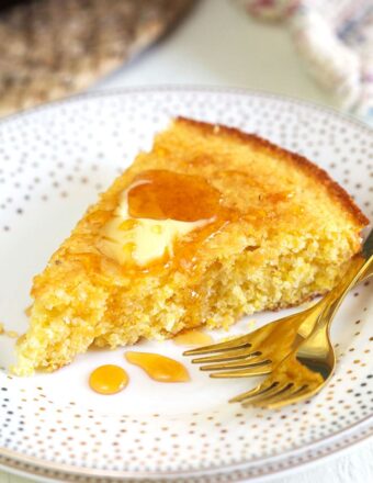 A piece of cornbread is garnished with butter and honey on a white plate.