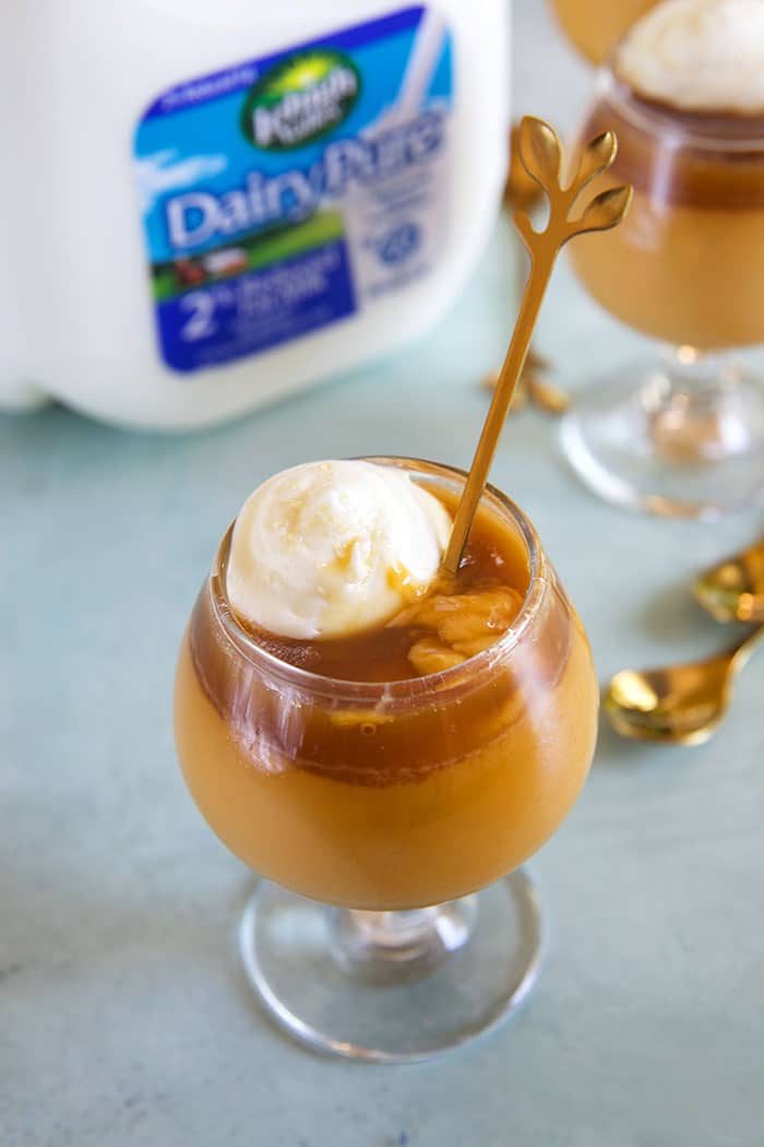 Butterscotch Pot de Creme in glasses on a blue board with a gallon of milk in the background.
