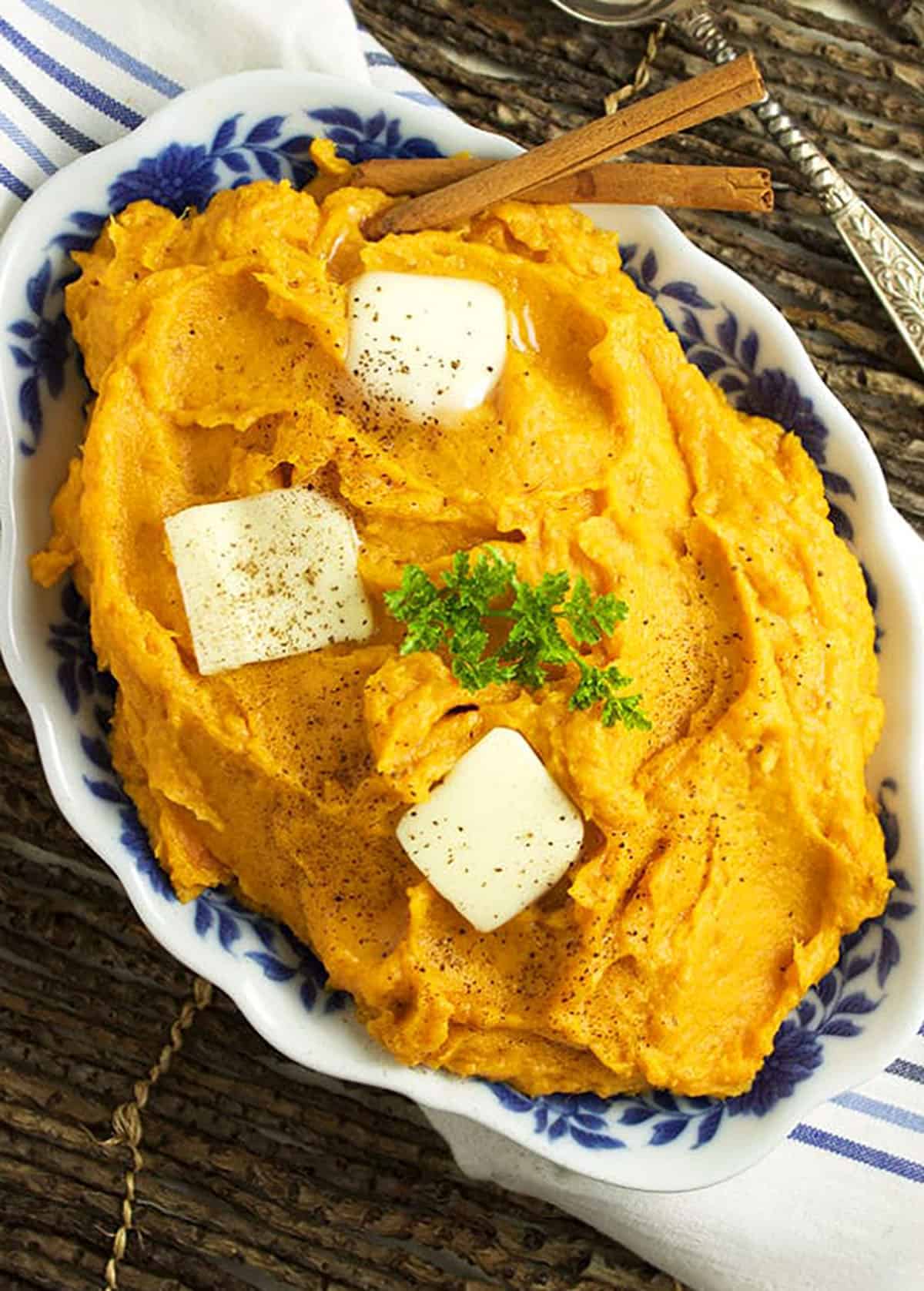 overhead of mashed sweet potatoes with three pats of butter and cinnamon sticks on top.