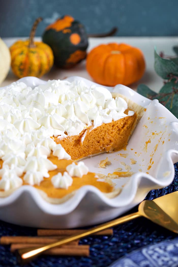Pumpkin chiffon pie in a white pie plate with pumpkins in the background.