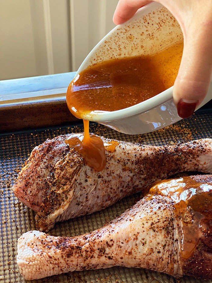 A brown mixture of maple syrup and butter is being poured onto an uncooked turkey leg.