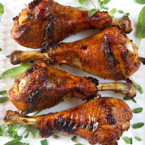 Four roasted turkey legs are on a white plate.