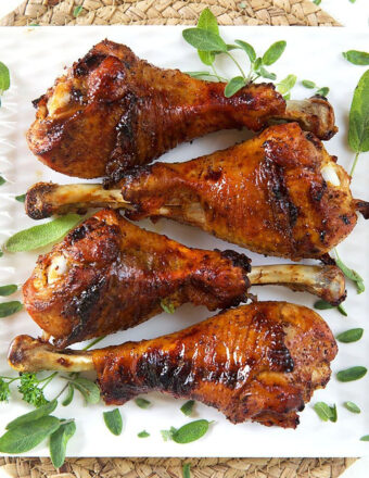 Four roasted turkey legs are on a white plate.