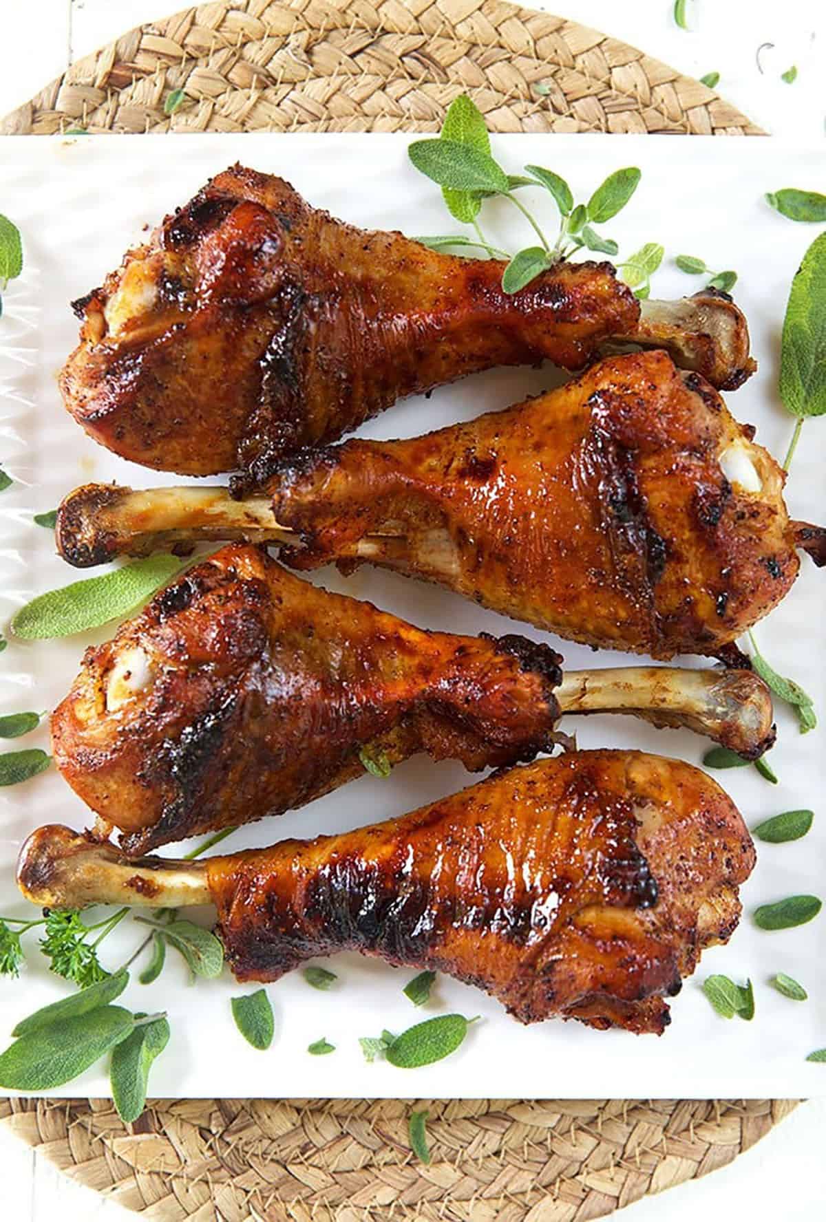 Four roasted turkey legs are on a white plate.