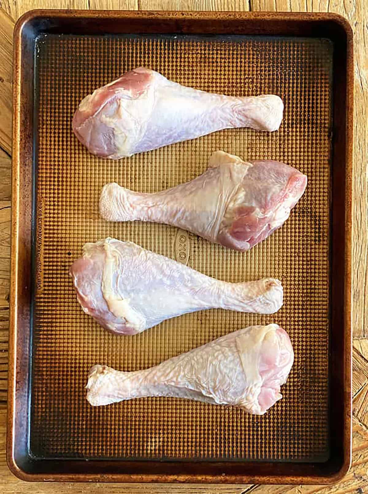 Four uncooked turkey legs are placed on a baking sheet.