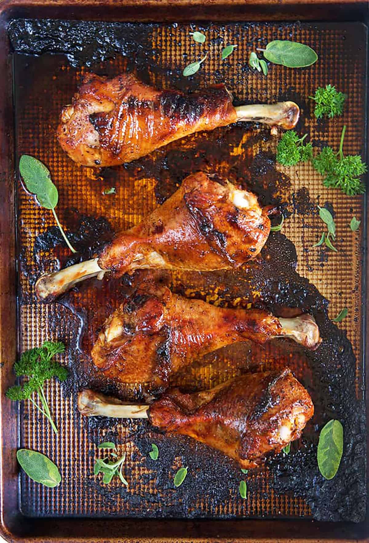 Four roasted turkey legs are on a baking sheet.