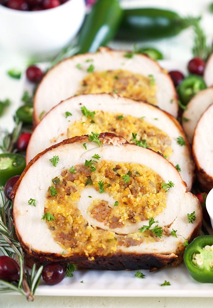 Turkey roulade sliced on a white plate with rosemary and cranberries.