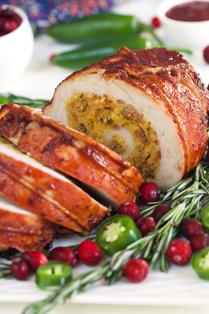 Turkey Roulade sliced on a white platter with rosemary and cranberries.