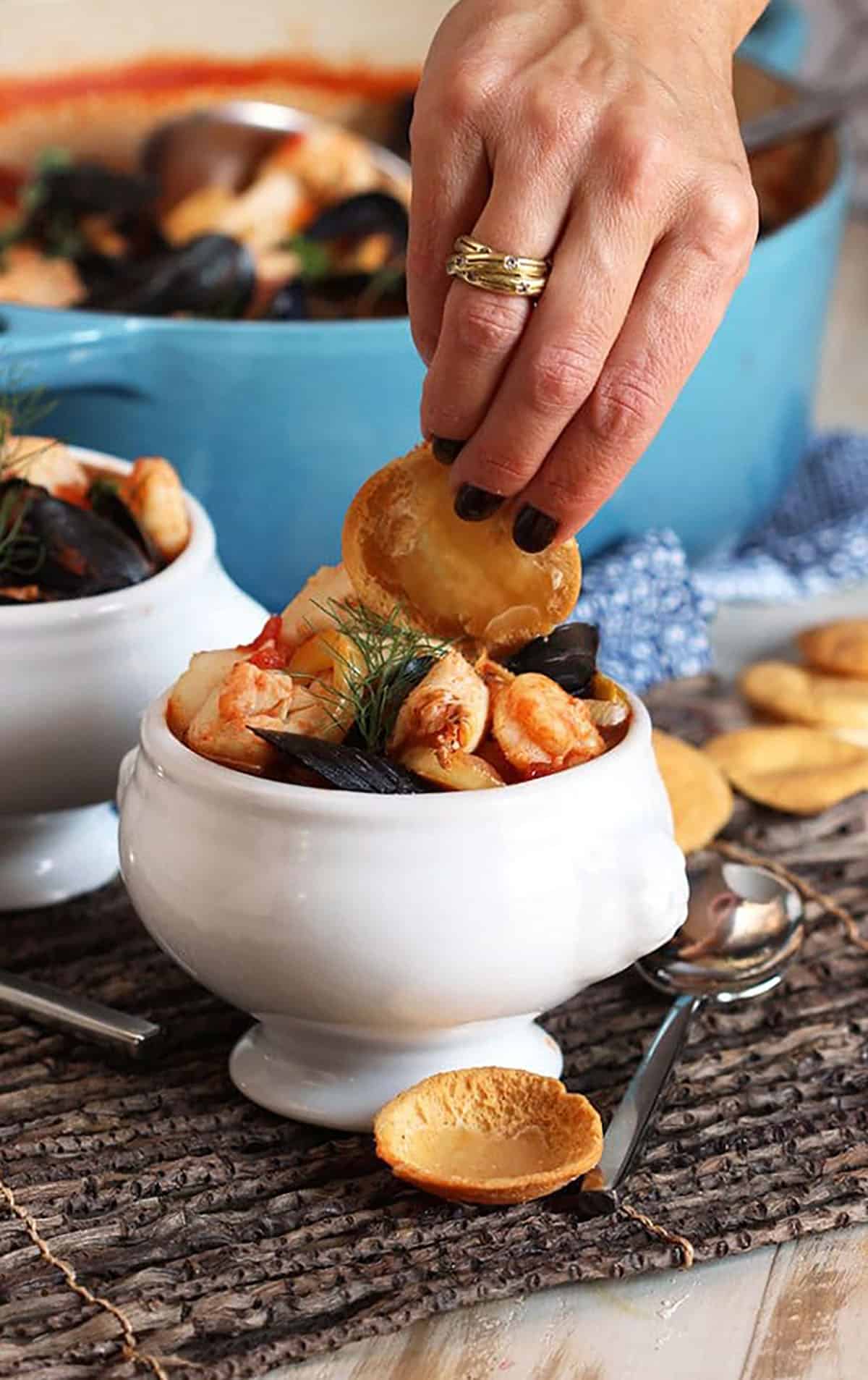 Hand dipping a chip in a bowl of bouillabaisse.