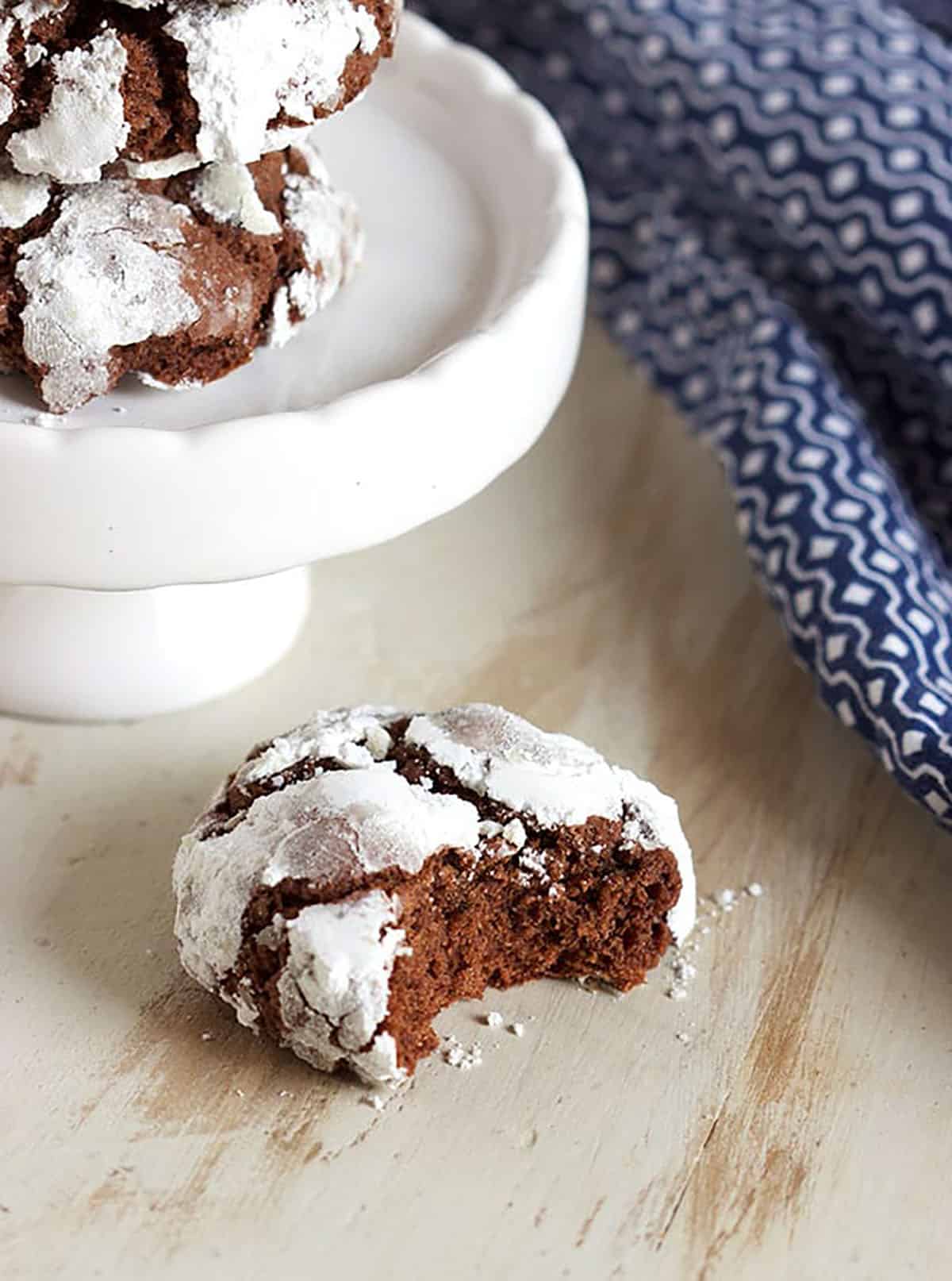 chocolate crinkle cookie with a bite taken on a white wood backdrop