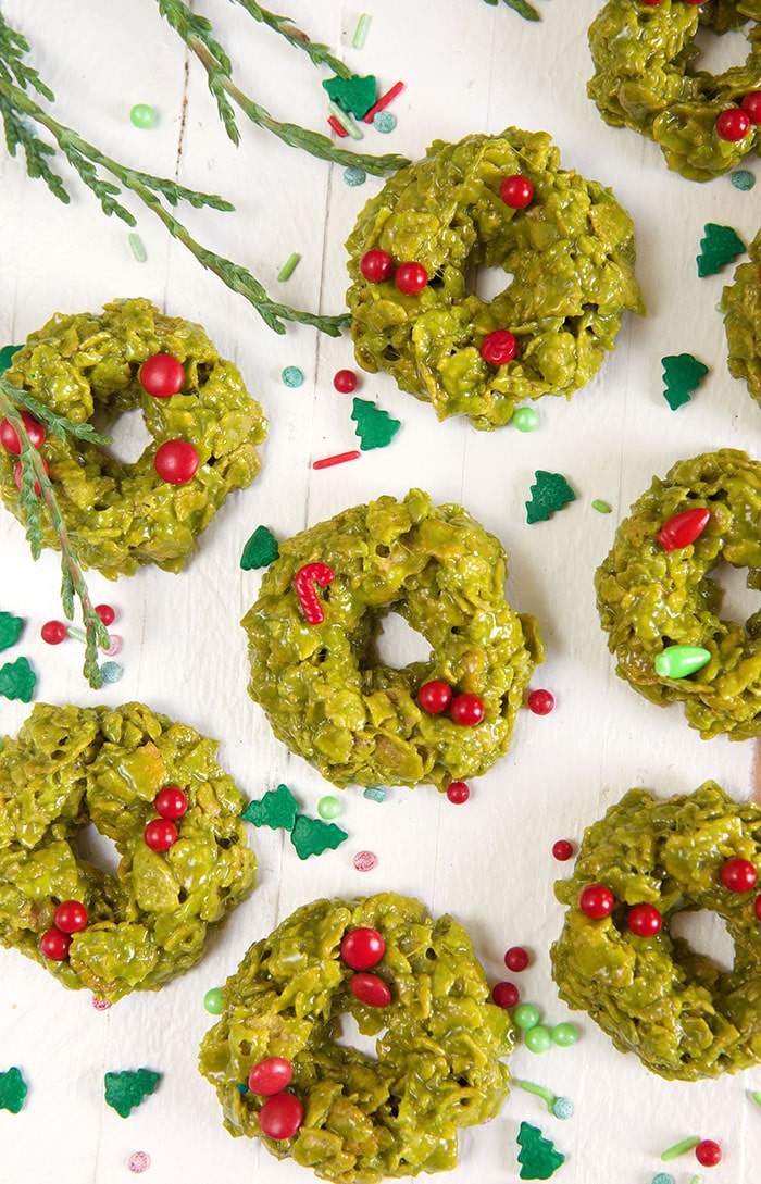 Multiple green cornflake wreath cookies are spread out on a white surface.