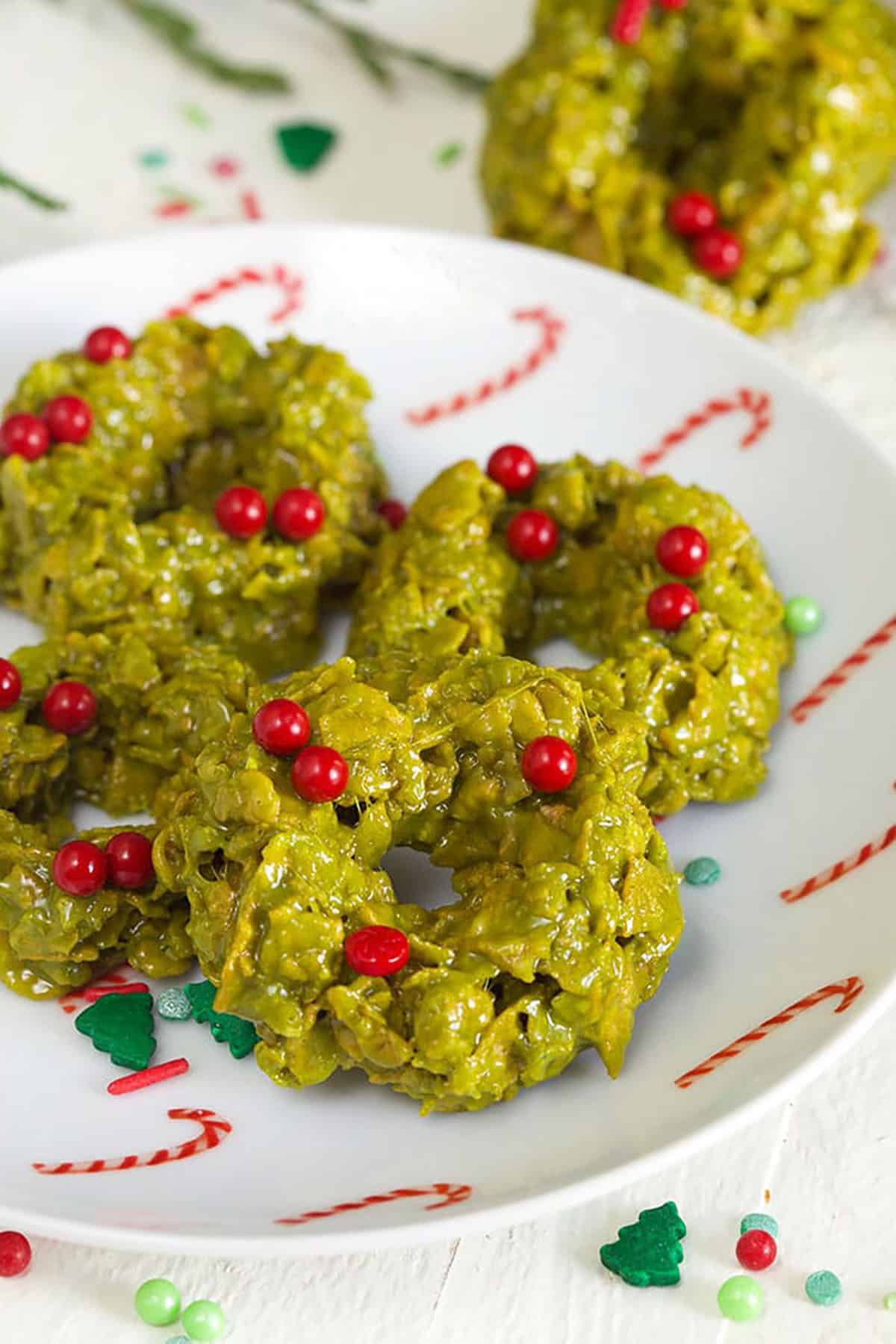 A white plate with candy cane presents a stack of green cookies.