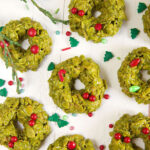 Multiple green cornflake wreath cookies are spread out on a white surface.