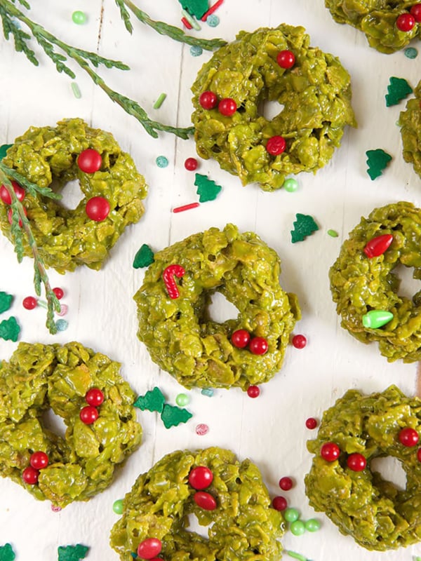 Multiple green cornflake wreath cookies are spread out on a white surface.