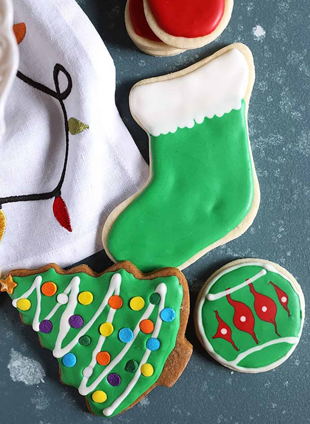 Overhead shot of a green stocking cookie and christmas tree cookie on a blue background.