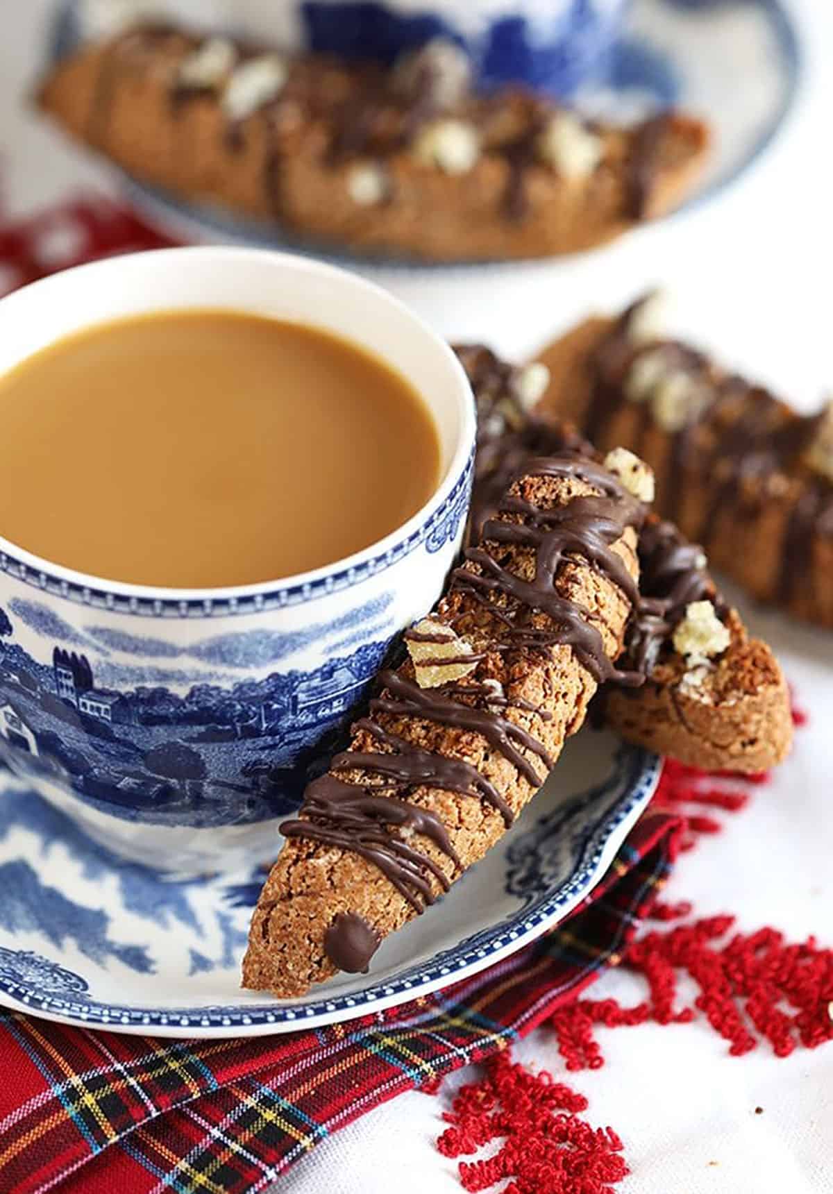 Gingerbread Biscotti on the side of a saucer with a cup of coffee.