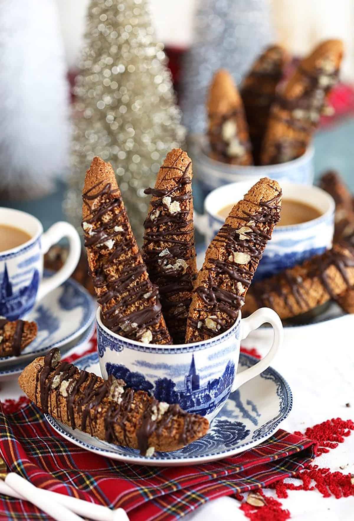 Gingerbread Biscotti with chocolate and crystalized ginger in a blue and white mug on a red plaid napkin.