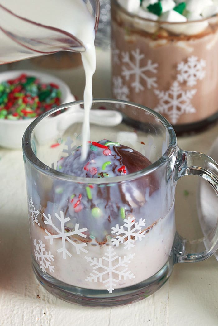 Milk being poured over a hot chocolate bomb in a glass.