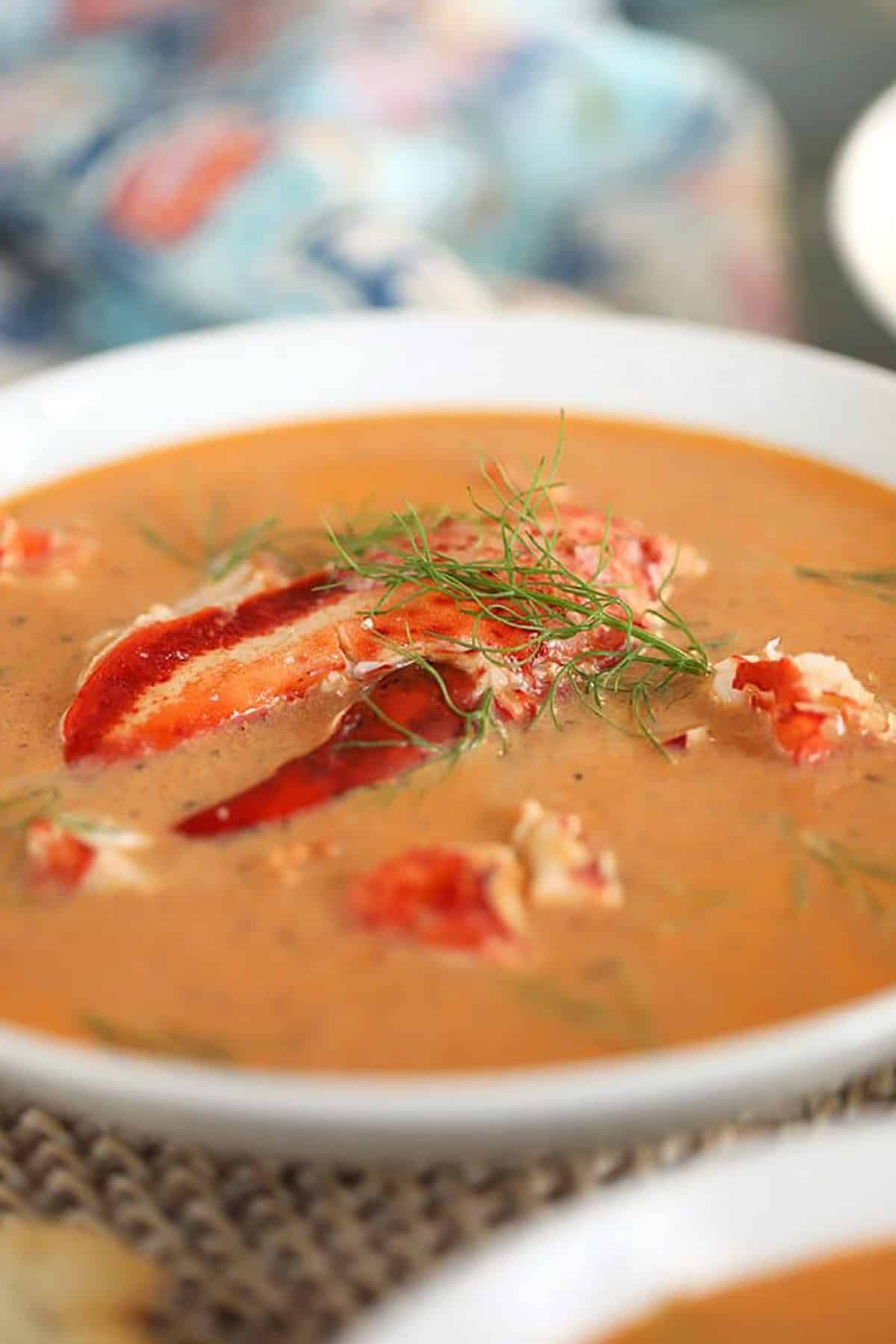 Close up shot of lobster bisque in a white bowl with a lobster claw in the center of the bowl.