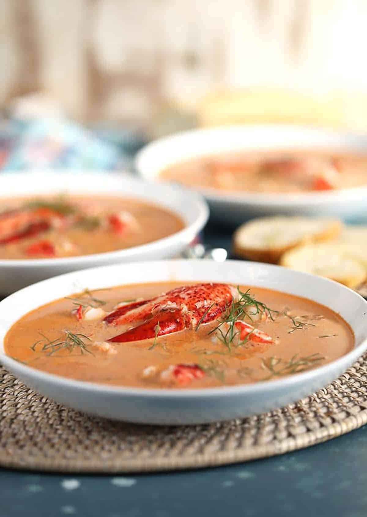Three white bowls with lobster bisque on a white placemat.